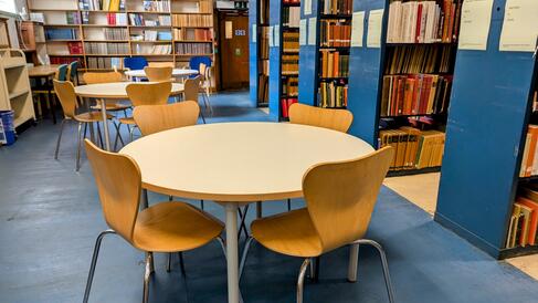 A large open room with round tables and chair surrounded by lots of bookshelves