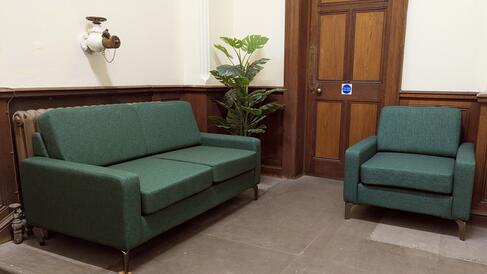 A large green sofa and a smaller green armchair on a stone floored landing