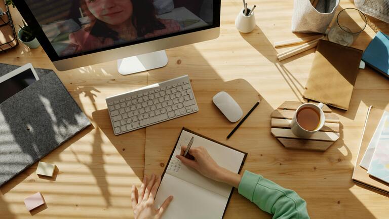 An overhead shot of someone working at a desk with a computer, lots of notebooks and a cup of coffee nearby